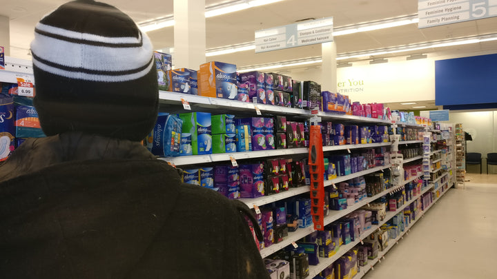 Postpartum caregiver dad standing in feminine hygiene aisle with pads for miles